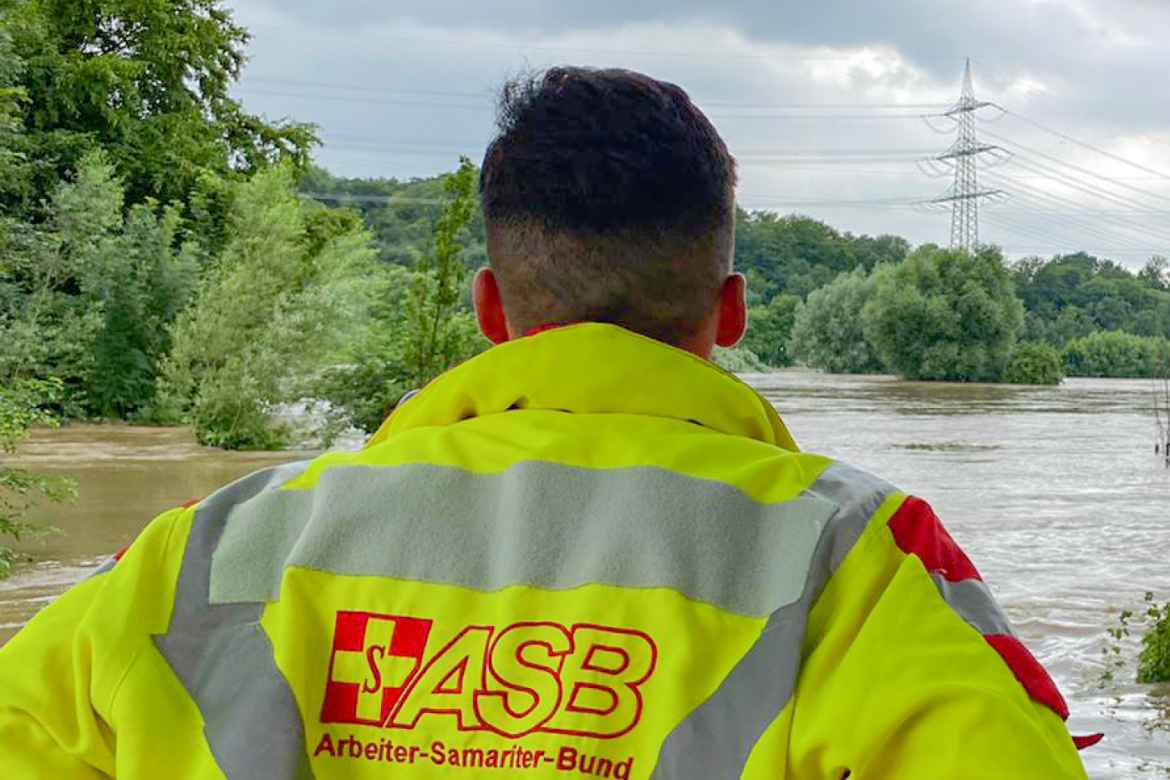 Ein Helfer des ASB schaut fassungslos über eine Hochwasserfläche.